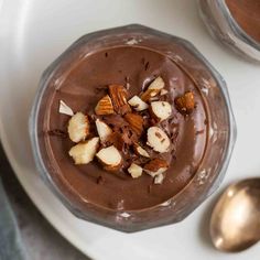 a bowl filled with chocolate pudding and nuts on top of a white plate next to two spoons