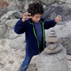 a young boy standing next to a pile of rocks