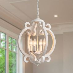 a white chandelier hanging from a ceiling in a room with windows and curtains