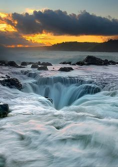 the sun is setting over an ocean with waves crashing on rocks and water flowing down it