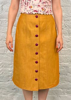 a woman standing in front of a white wall wearing a yellow skirt with buttons on the side