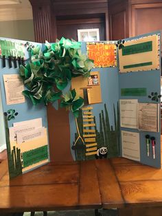 an open book on a wooden table with paper cut outs and green trees in the middle