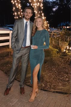 a man and woman standing next to each other in front of a tree with lights