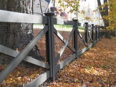 a fence that is next to a tree with leaves on the ground in front of it