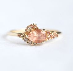 a close up of a ring with an oval shaped peach sapphire and two smaller round diamonds