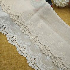 three pieces of white lace sitting on top of a yellow tablecloth next to flowers