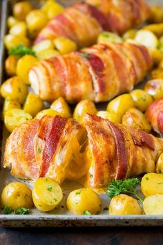 bacon wrapped stuffed chicken on a baking sheet with potatoes and parsley in the background