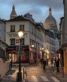 people are walking down the street in an old european town at night time with lights on