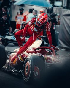 a man in red racing suit leaning over the side of a race car