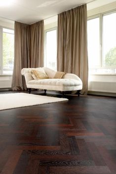 a living room with wooden floors and large windows in the corner, along with a white rug on the floor