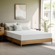 a white bed in a bedroom next to a wooden dresser and window with an art piece on the wall