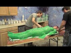 two men working on a large green object in a room with wooden cabinets and counter tops