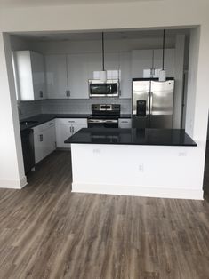 an empty kitchen with white cabinets and black counter tops, stainless steel appliances and wood flooring