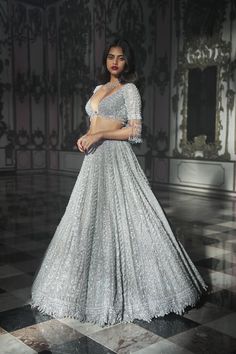 Make a starry entrance with this luxurious grey tulle lehenga set. Ornately stitched ensemble is encrusted with a pool of sequins, stones and diamante embroidery all over giving it a glamourous and opulent look. The sparkly skirt is beautifully complimented with a tasselled blouse and a sheer net matching dupatta. This picturesque ensemble will surely steal glares.  Available at BIBI London. To book your appointment, call us at 07931 999111. Tulle Lehenga, Lehenga For Girls, Sangeet Lehenga, Seema Gujral, Kurta Lehenga, Sparkly Skirt, Raw Silk Lehenga, Tonal Embroidery, Wedding Inside