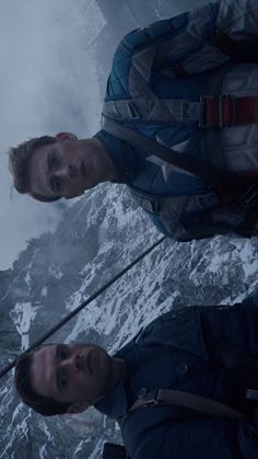 two men standing next to each other in front of snow covered mountains