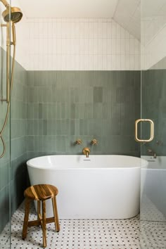 a white bath tub sitting next to a shower and a wooden stool in a bathroom