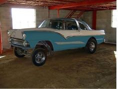 an old blue and white car is parked in a garage with red beams on the ceiling