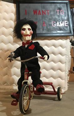 a creepy doll is riding a tricycle in front of a sign that says i want to play a game