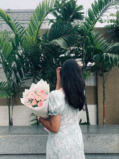 a woman in a white dress holding a bouquet of flowers and looking at palm trees