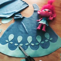 a pink troll doll sitting on top of a blue piece of paper next to scissors