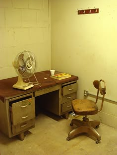 an old wooden desk with a fan on top of it and a chair next to it