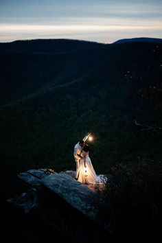 a bride and groom standing on top of a mountain at night