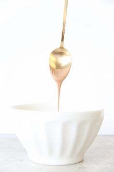 a gold spoon in a white bowl filled with liquid