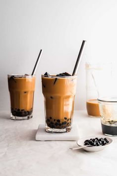 two glasses filled with iced coffee on top of a white counter next to chocolate chips