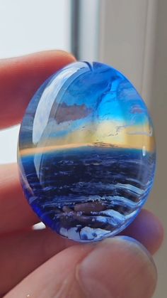 a hand holding a glass ball with an image of the ocean and sky in it