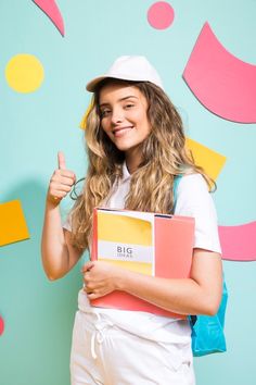 a young woman is holding a folder and giving the thumbs up while standing in front of a colorful background