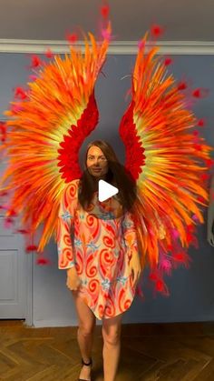 a woman is standing in front of a blue wall with an orange and red feathered costume on