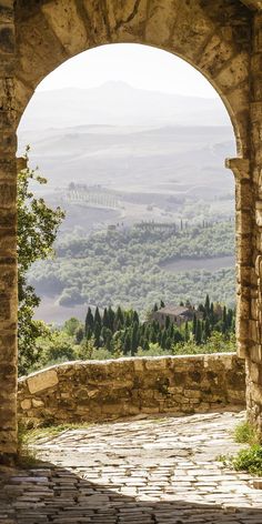 an arch in the side of a stone building with trees and hills in the background