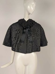 VICTORIAN 19TH C BLACK BROCADE SILK CAPE W CHANGEABLE LINING DATING TO THE VICTORIAN 19TH CENTURY FASHIONED OF A BLACK SILK RICH BROCADE WITH TWO ROWS OF BLACK CHANTILLY LACE RUFFLES ENCIRCLING THE NECKLINE.   SILK SATIN RIBBONS TRIM THE FRONT WITH A BOW AT THE NECKLINE AND THE INTERIOR IS IN A PURPLE AND GREEN CHANGEABLE SILK.   CONDITION:  THERE IS A SMALL FRAY AT THE CENTER REAR OF THE LINING AS WELL AS SOME FRAY AT THE CENTER REAR TOP NECKLINE IN THE LINING.   THE EXTERIOR HAS NO FLAWS, I WO Victorian Black Formal Outerwear, Black Historical Design Outerwear For Costume, Silk Cape With Cape Sleeves For Formal Occasions, Formal Black Capelet, Black Capelet For Costume, Elegant Black Capelet With Cape Sleeves, Formal Black Cape With Cape Sleeves, Black Cape For Evening Wear, Elegant Black Cape For Costume