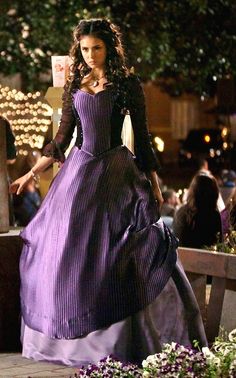 a woman in a long purple dress is standing on a wooden bench with lights behind her