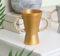 a gold cup sitting on top of a white table next to a potted plant