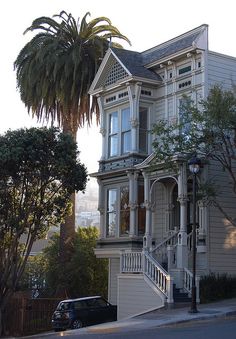 an old victorian house with a palm tree in the foreground and a car parked on the street