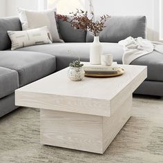 a white coffee table sitting in front of a gray couch with pillows on top of it