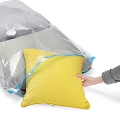 a person holding a yellow pillow in front of a plastic bag