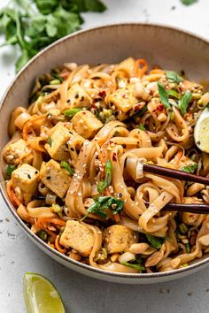 a bowl filled with noodles, vegetables and tofu on top of a white table