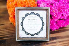 the wedding stationery is surrounded by pink and orange carnations, which are also in bloom