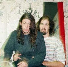 two men sitting next to each other in front of a wall with writing on it