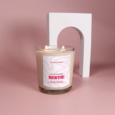 a white candle sitting in front of a wooden block with the word bestie on it