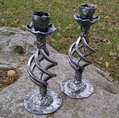 two metal candlesticks sitting on top of a rock