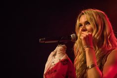 a woman with long blonde hair holding a microphone in her hand and singing into the microphone