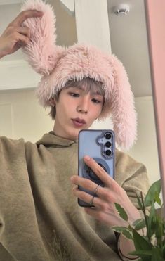 a woman taking a selfie in front of a mirror wearing a fuzzy pink hat