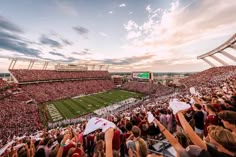 a football stadium filled with people watching the sun go down and fans holding up their hands