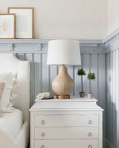 a white dresser with a lamp on top of it next to a bed in a bedroom