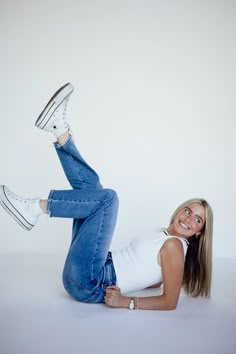 a woman in white shirt and jeans laying on the ground with her legs spread out