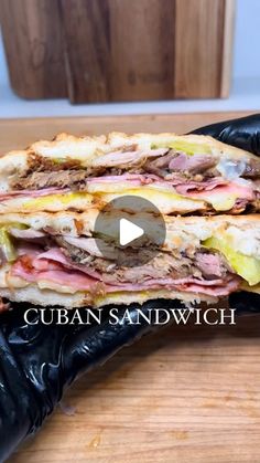 a large sandwich cut in half on top of a wooden table with black plastic gloves