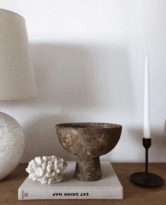 a table topped with a lamp next to a book and a bowl on top of it